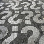 White question marks painted on asphalt in a pattern, alternating between upside down and right-side up