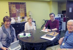 John Pletscher, accompanied by his daughter Chris, is interviewed by Tom Piltoff while Debbie Peterson transcribes