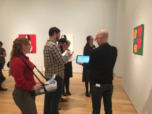 Cathy Rajcan, on left, writes on her steno machine, which is strapped to her with a harness. At right, a tour guide talks about a piece of art for a museum guest.