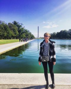 A young blond woman standing in front of the reflection pool with the Washington Monument in the background