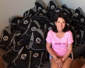 A smiling woman sits in front of a pile of black backpacks