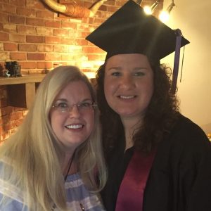 Two women stand side by side, one in a graduation cap and gown