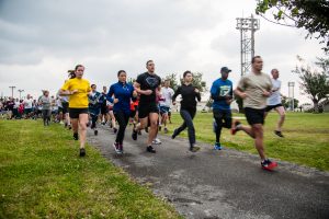 Runners wearing athletic apparal in a race down a narrow paved road with grass on either side