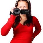 Girl holding a camcorder in front of her face; she seems to be smiling