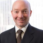 Headshot of an NCRF Major Gifts donor: a man in a suit in front of an office window with an urban background