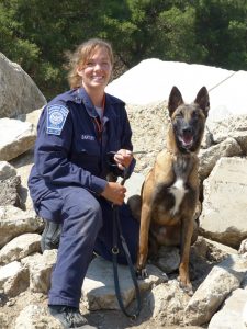 A woman in uniform poses, kneeling, next to a german shepherd mix dog on a leash