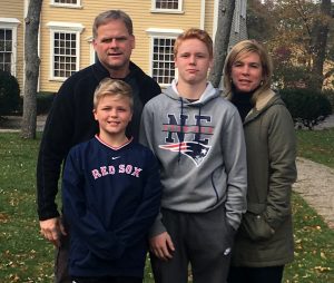 A family of four dressed for chilly weather pose outside in front of a suburban house