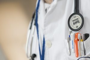 Close-up view of doctor's lab coat with a stethoscope around the doctor's neck and and collection of pens in the pocket