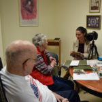 Kerry Ward, far right, liaison specialist for the Library of Congress Veterans History Project (VHP), reads postcards sent home by U.S. Veteran Don Shearer, who was a German prisoner of war during World War II. Shearer’s wife, Martha, shared his story and artifacts for the Ginger Cove VHP.