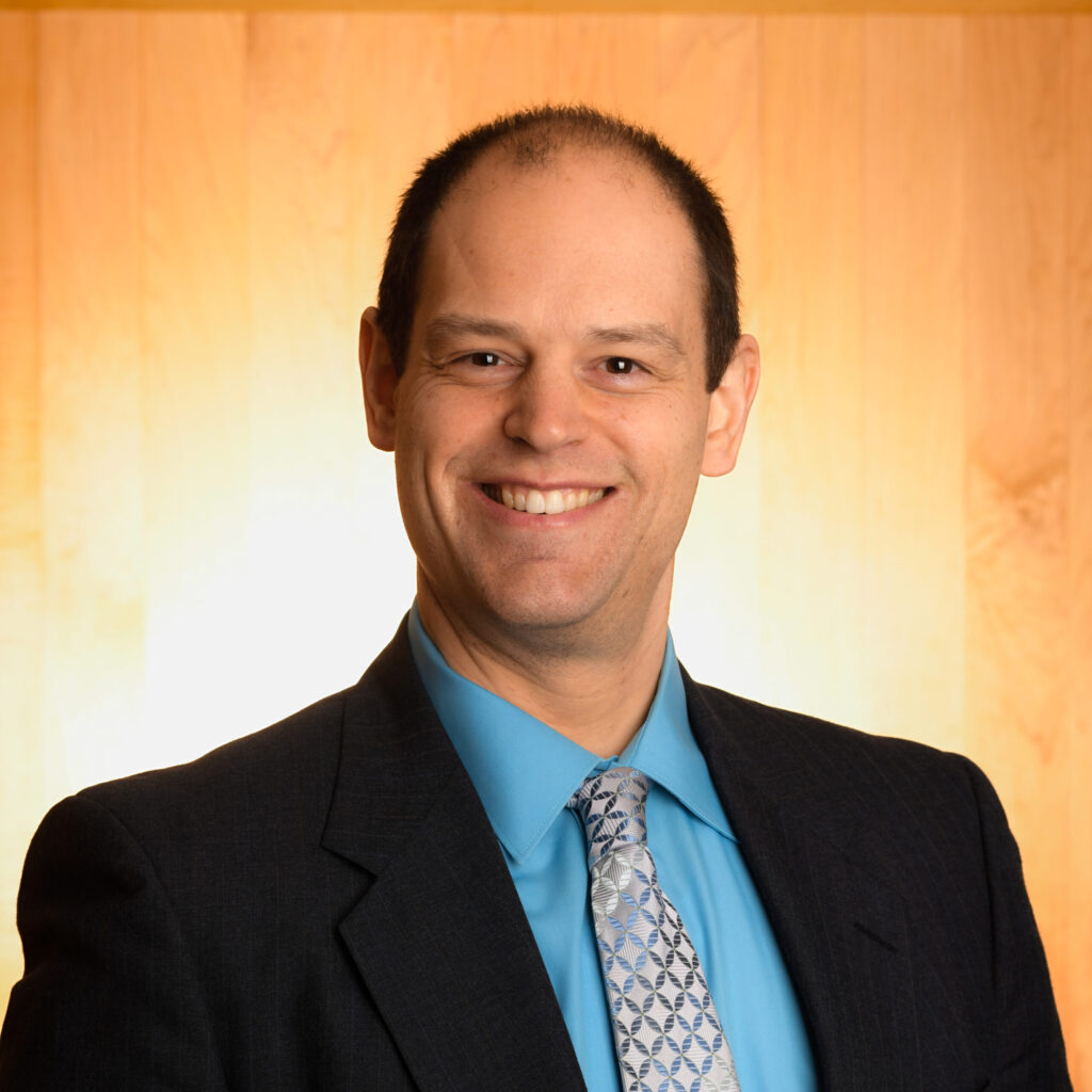 Professional headshot of man in a suit and tie smiling at the camera