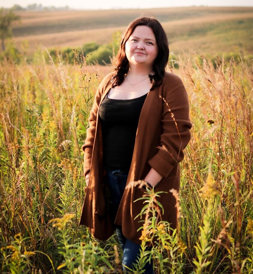 Woman standing in a field smiling at the cameral