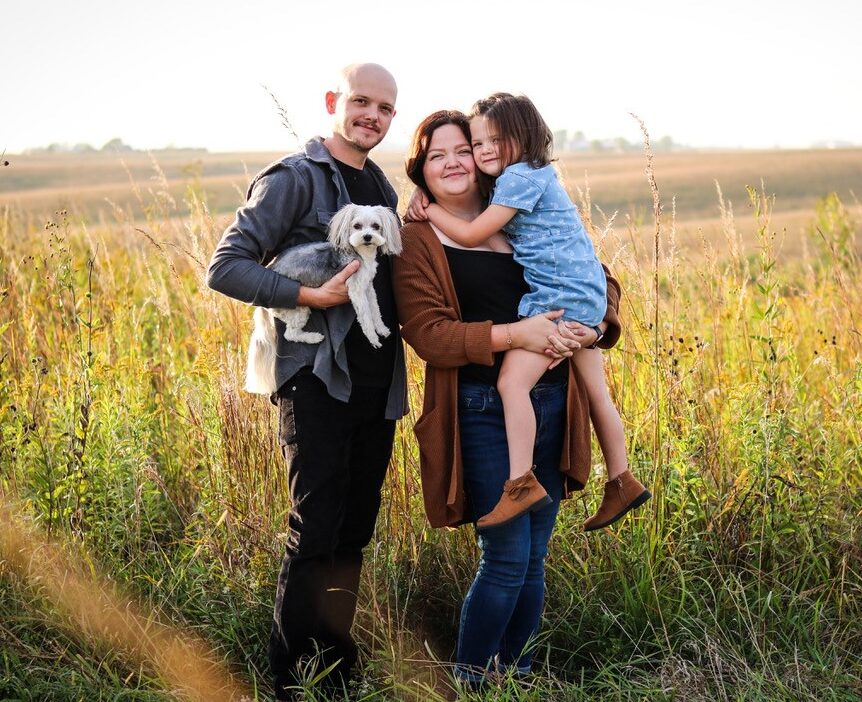 A family with their dog standng in a field posing for the camera