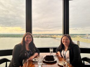 Two women seated at a restaurant table smiling at the camera with the Ohio RIver in the background
