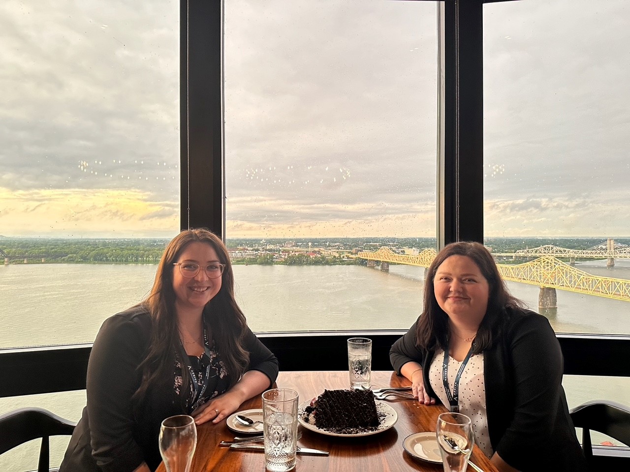 Two women seated at a restaurant table smiling at the camera with the Ohio RIver in the background
