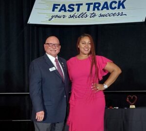 Denee Vadell and Doug Friend pose together at an event under a banner reading 'Fast Track your skills to success.