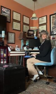 Woman sitting in a home office writing at a steno machine and smilng at the camera