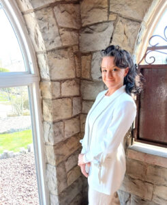 Woman in a white pantsuit standing in front of a window and smiling at the camera