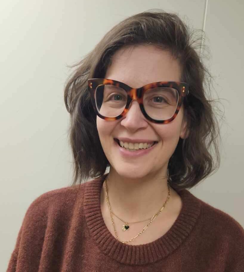 Woman in glasses and a brown sweater smiling at the camera