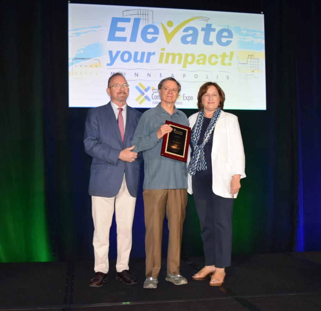 A man on a stage accepting an award from a man and a woman