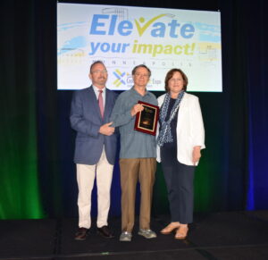 A man on a stage accepting an award from a man and a woman