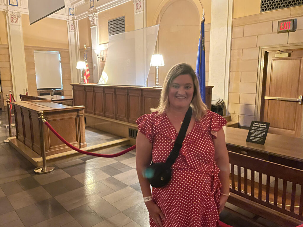 Blonde woman in a red dress standing in a courtroom and smiling at the camera