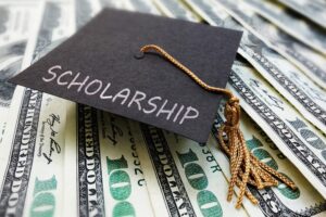 Graduation hat with the word scholarship written on top - lying on a bed of hundred dollar bills
