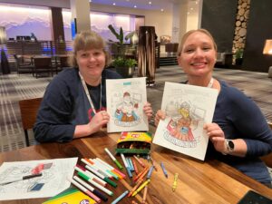 Two women holding up pages from a coloring book and smiling at the camera