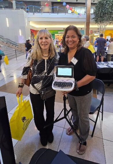 Two women posing for the camera and holding a steno machine