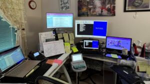 A home office with several computer monitors, keyboards, and a steno machine
