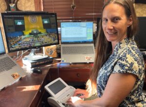 A woman writing on a steno machine with computer monitors in the background
