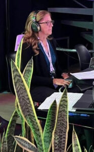 A woman writing on a steno machine with a plant in the foreground
