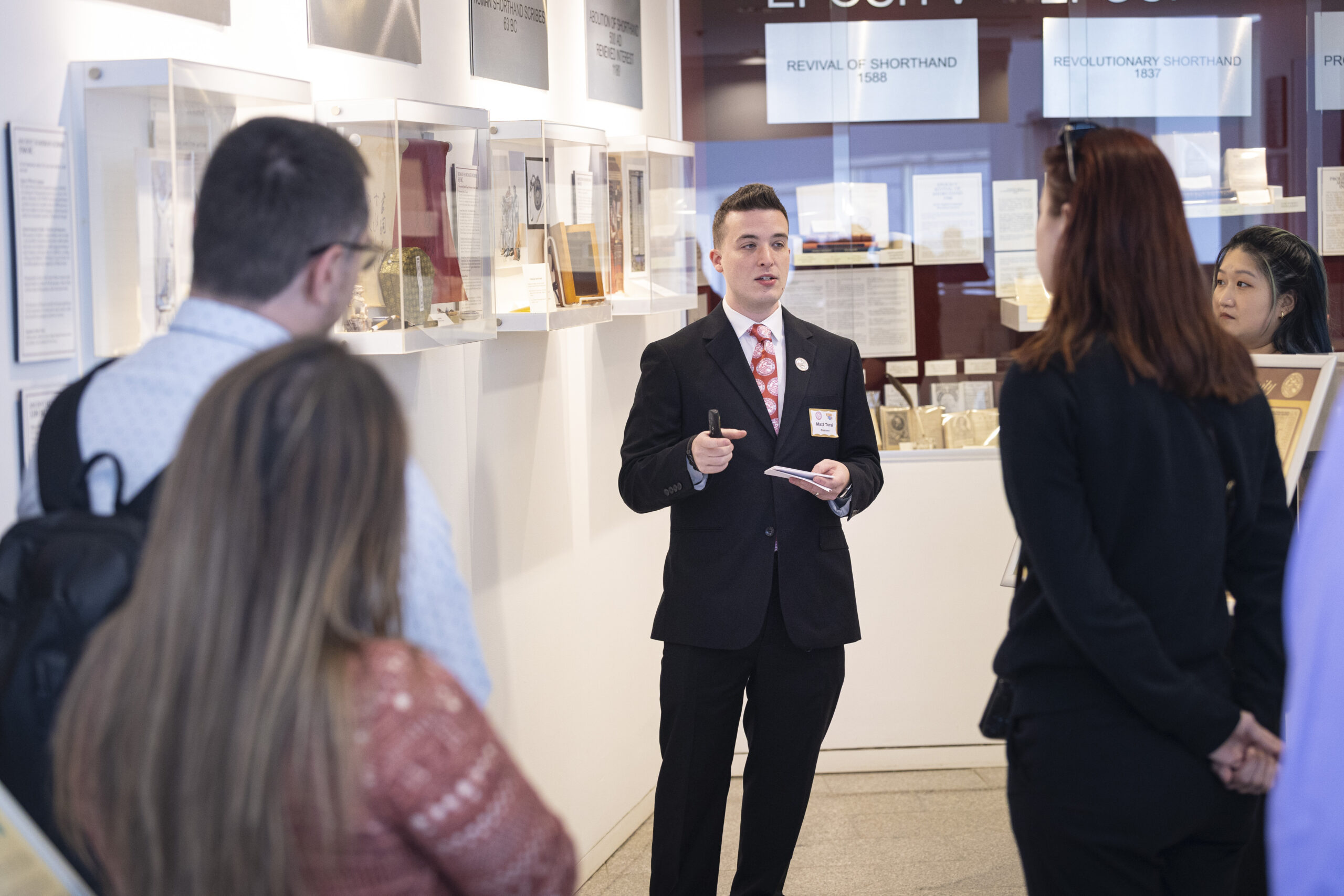 A man standing in a museum talking to a group of people