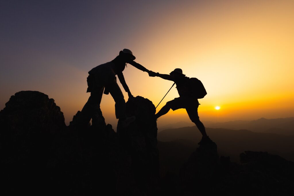 a silhouette of two people helping each other on a hike at sunset