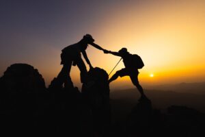a silhouette of two people helping each other on a hike at sunset